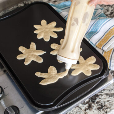 Pancake Dispenser creating pancake floral designs on griddle on stovetop