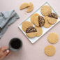 Plain and chocolate dipped geo stamped cookies on a plate, hand holding coffee.