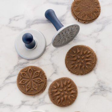 Raw gingerbread cookie dough with three Nordic Ware cookie stamp impressions showing star, snowflake, and tree designs