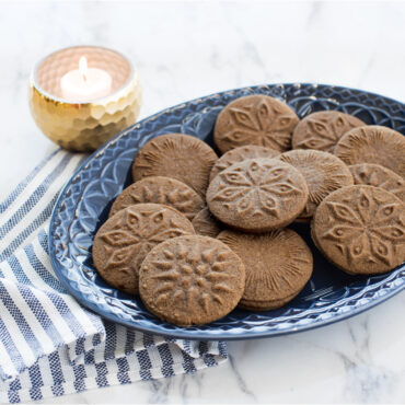Golden baked cookies with celestial star and moon impressions arranged on white plate, made with Nordic Ware cookie stamps