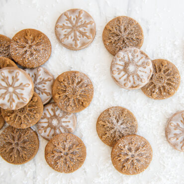 Golden baked gingerbread cookies displaying detailed snowflake patterns from Nordic Ware cookie stamps, dusted with powdered sugar