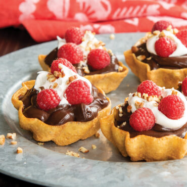 Three golden timbale shells filled with chocolate pudding, whipped cream, and fresh raspberries on white plate