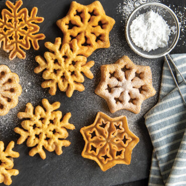 Golden-brown rosette pastries dusted with powdered sugar arranged on dark surface, showing delicate flower-like shape