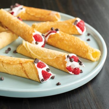 Filled krumkake with cream, raspberries and chocolate chips on a plate