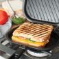 Open grill press on stovetop with grilled sandwich