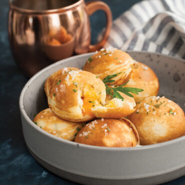 Cast iron ebelskiver pan with seven round wells, filled with golden-brown Danish pancake balls, some with melted cheese