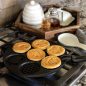 Bee Pancake Pan on stovetop with 5 cooked pancakes in cavities, syrup and butter on the side counter