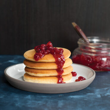 Stack of golden mini pancakes topped with red lingonberry jam, made using Nordic Ware silver dollar pancake pan