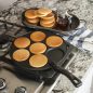 Cooked plain pancakes on pancake pan on stovetop, stack of pancakes on plate on counter.
