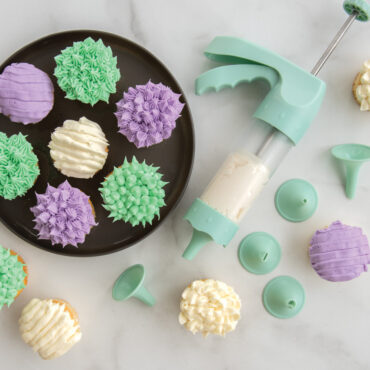 Six cupcakes with elaborate white frosting decorations made using Nordic Ware decorating tips and spritz maker