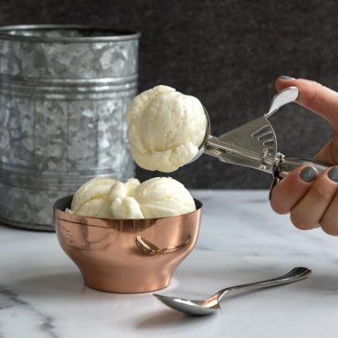 Hand scooping ice cream with Large cookie scoop into bowl.