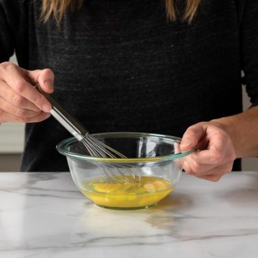 Small whisk being used to whisk eggs in a small bowl.