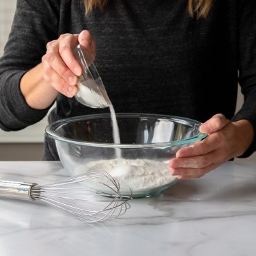 Dry ingredients in a large glass mixing bowl, large whisk on the counter.