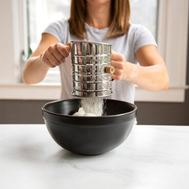 Flour Sifter in use, woman sifting flour into mixing bowl.