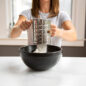 Flour Sifter in use, woman sifting flour into mixing bowl.