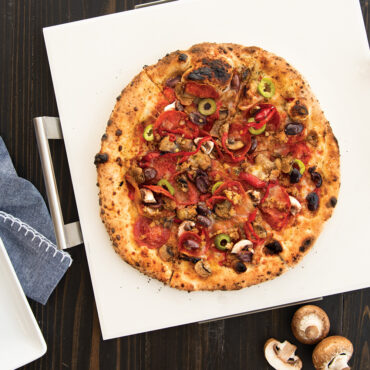 Golden baked pizza with melted cheese and toppings on Nordic Ware square ceramic pizza stone with metal rack