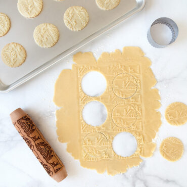 Woodland cottage embossed rolling pin with decorated dough cutouts and golden baked cookies showing detailed pattern