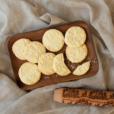 Golden embossed cookies with woodland cottage designs arranged on white serving platter