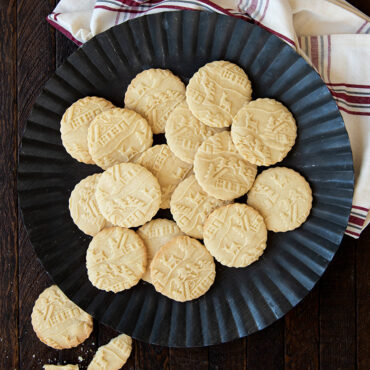 Golden baked cookies with woodland cottage embossed designs arranged on white plate beside red holiday towel