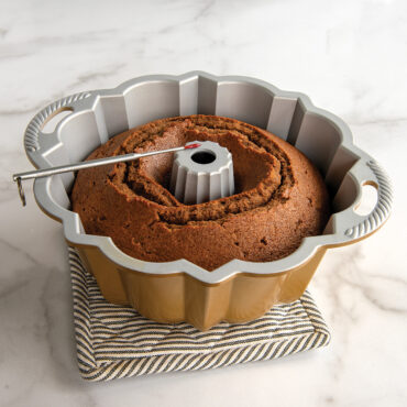 Red digital thermometer probe inserted into golden-brown bundt cake in fluted aluminum bundt pan