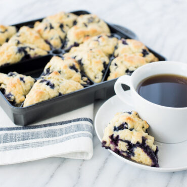Nordic Ware aluminum Scottish mini scone pan with six golden-brown baked scones and black coffee cup