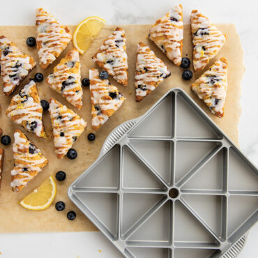 Golden baked mini scones on parchment beside Nordic Ware aluminum Scottish mini scone pan showing triangular cavities