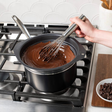 Nonstick double boiler inside a sauce pan on the stovetop with melted chocolate and hand mixing with a whisk