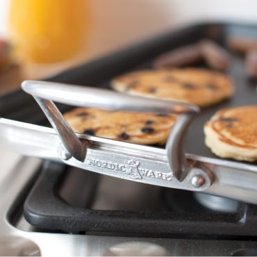 Closeup of griddle handles, griddle on stovetop with pancakes
