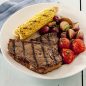 steak, corn on the cob, roasted tomatoes and potatoes on plate