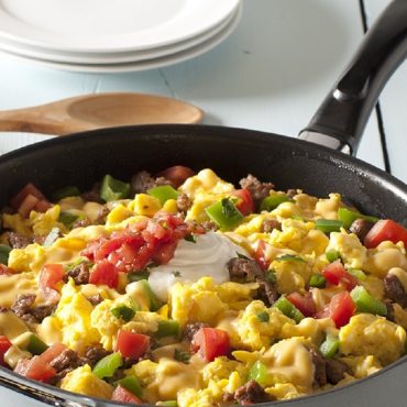 Skillet filled with scrambled eggs, pepper, sausage, salsa, sour cream
