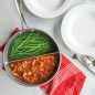 Stew and green beans in divided sauce pan with dinner plates