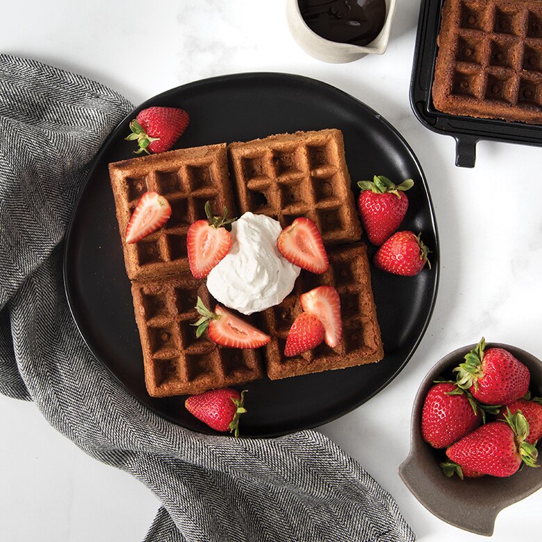 Plated chocolate waffles with whipped cream and strawberries