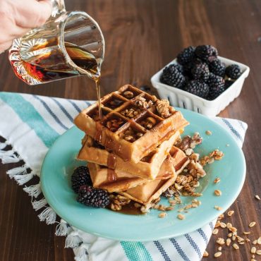 Maple syrup pouring over stack of waffles