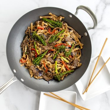 Stir fry noodles with beef and vegetables in 14" Spun Wok, plates on the side.
