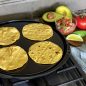 Corn tortillas on flat side of griddle on stovetop, heating