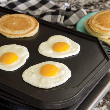Nordic Ware aluminum reversible griddle on stovetop with fried eggs and golden pancakes on flat side