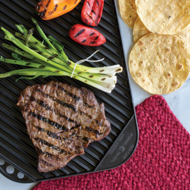 Grilled steak and sautéed peppers and onions on Nordic Ware reversible griddle with grill ridges, tortillas alongside