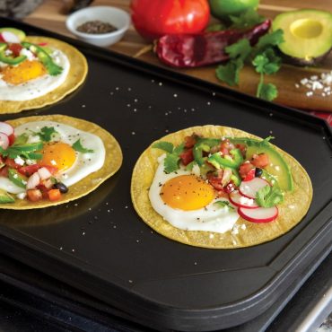 Breakfast tacos on griddle flat side with avocado, fried egg, and salsa