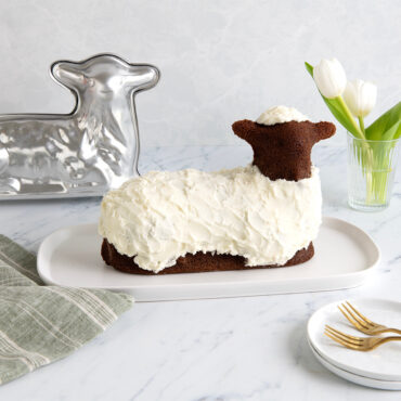 Chocolate lamb-shaped cake on white plate next to Nordic Ware 3D lamb cake pan, cast aluminum with detailed texture