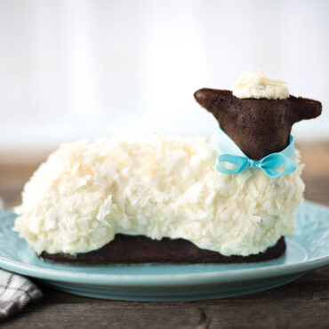 Nordic Ware 3D lamb cake pan with baked chocolate lamb cake decorated with white ribbon on white plate
