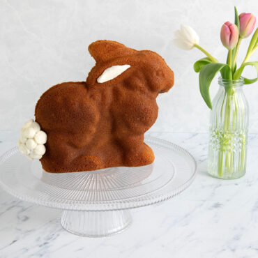 Golden bundt cake shaped like a sitting bunny on white cake stand, showing detailed texture from Nordic Ware 3D mold