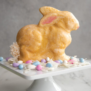 Golden glazed bunny-shaped cake baked in Nordic Ware 3D bunny cake pan, standing upright on white cake stand