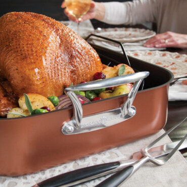 Golden roasted turkey in Nordic Ware extra-large copper roaster with carving knife and fork beside pan
