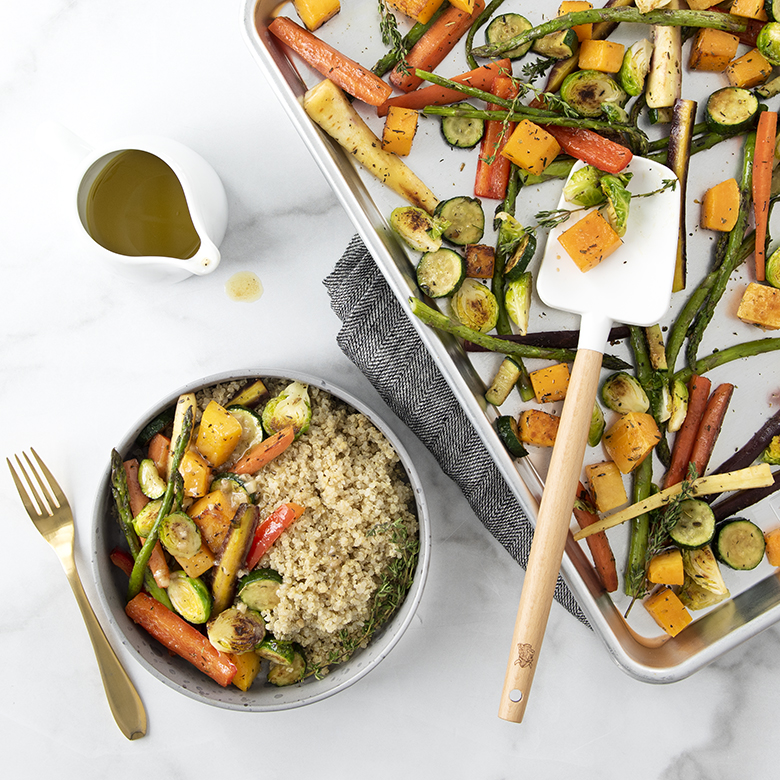 Image of veggie and quinoa bowl with honey mustard dressing next to a sheet pan with roasted vegetables