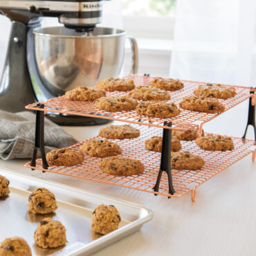 Nordic Ware stackable cooling grids with golden baked cookies, black legs, beside stand mixer and sheet pan