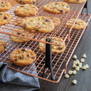 Freshly baked chocolate chip cookies cooling on Nordic Ware copper-colored stackable wire cooling grids