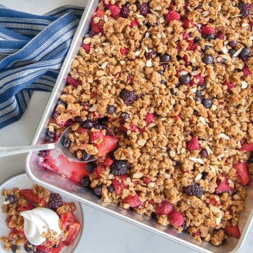 Baked fruit crumble in High Sided Sheet cake Pan, spoon scooping onto plate
