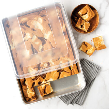 Nordic Ware aluminum high-sided sheet cake pan with clear lid, containing golden brown blondies