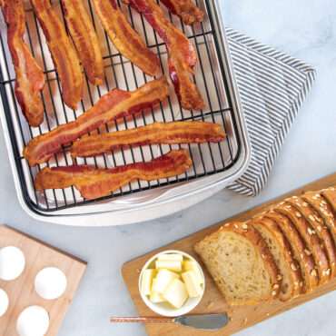 Crispy bacon strips on Nordic Ware aluminum oven crisp baking tray with wire rack, served with bread and eggs