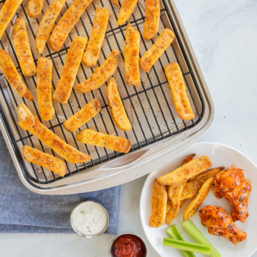 Golden baked potato fries on Nordic Ware aluminum baking tray with chicken wings and celery served alongside